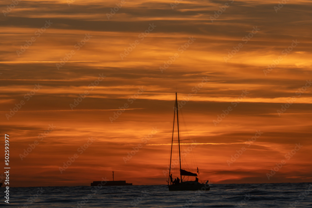 atardecer de verano en el mar con velero, espigón, hermoso sol y nubes de colores