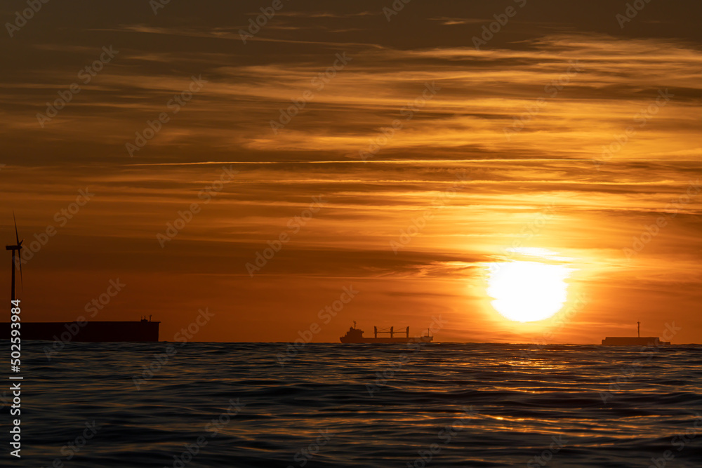 atardecer de verano en el mar con el sol espectacular y siluetas de barco, espigón y cielo de colores 