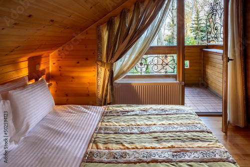 Cozy mansard bedroom with natural wood trim with double bed and balcony