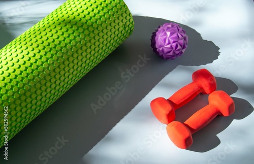 Multi-colored fitness accessories: sports roll, dumbbells on a blue surface with beautiful shadows. The concept of a healthy lifestyle, time to lose weight, home sports equipment.