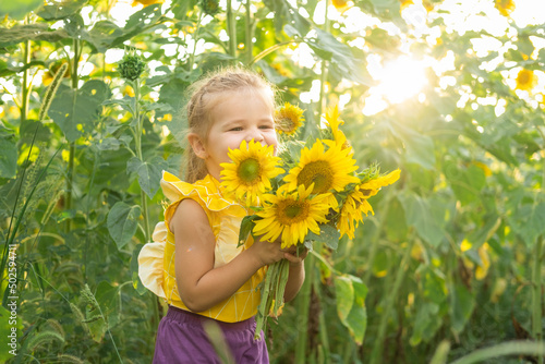 happy little kid girl playing in blooming sunflower field on sunny summer day