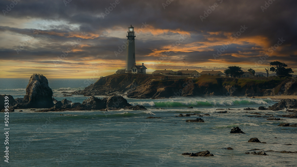 Pigeon Point Lighthouse under a cloudy sunset sky with waves crashing into the coastline rocks