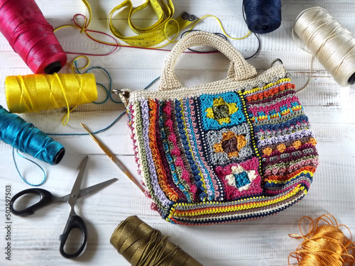 Crafting activity of making colorful crochet bag made of nylon yarn in various colors.  Tools and yarns appeared in frame, white wooden table as background. Focus selection.  photo