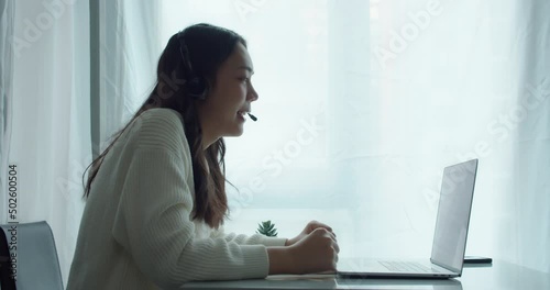 Close up of beautiful asian businesswoman wearing headphones for a videoference from home office.Female are student by webcam video call chat explain and take note course online at home.