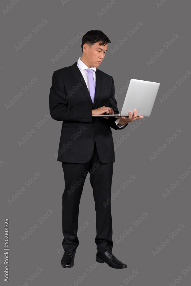 A businessmanwho works uses a laptop. while standing on a gray background A businessmanwho works uses a laptop. while standing on a gray background