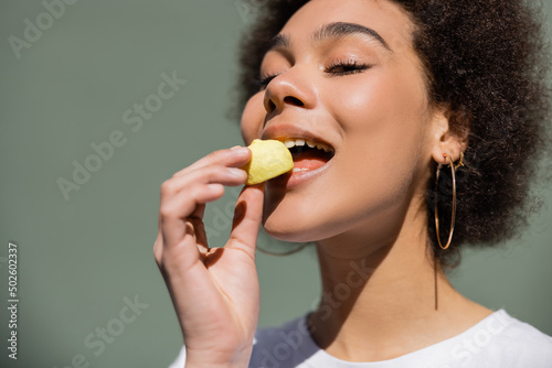 pleased african american woman eating yellow candy