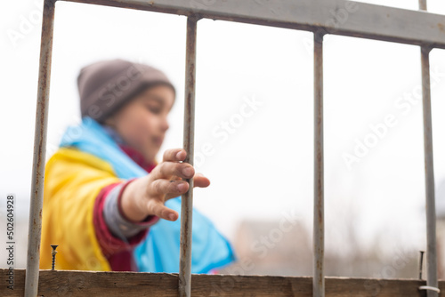 A little refugee girl with a sad look behind a metal fence. Social problem of refugees and internally displaced persons. Russia's war against the Ukrainian people photo