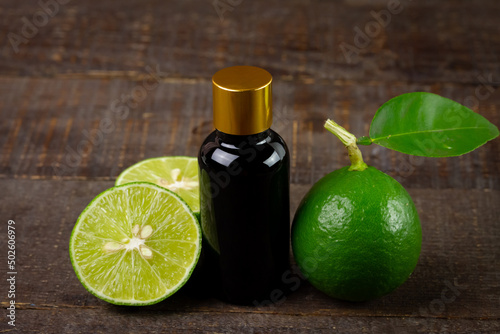 Lime essential oil in glass bottle and fresh lime fruits with green leaf on rustic wooden table. Use for spa, aromatherapy and bodycare concept.