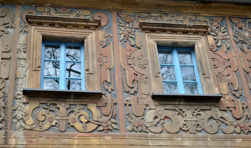 Zdjęcie architektury przedstawiające dwa okna w kamienicy pokrytej płaskorzeźbą
