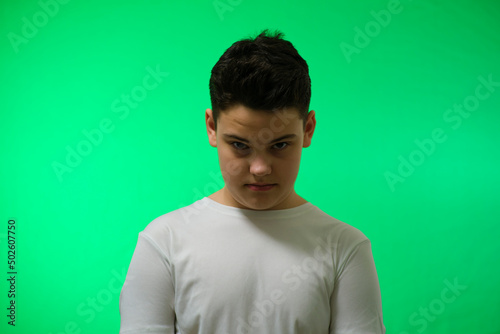 a 12-14 year old boy on a green background looks at the camera from under his forehead does not smile very angry