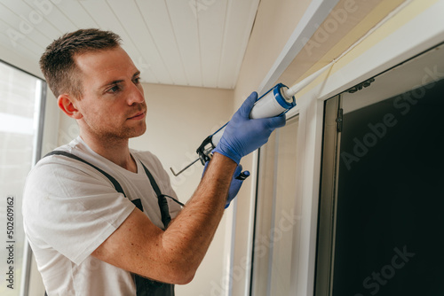 Young man wearing overalls sealing cracks between window and trim