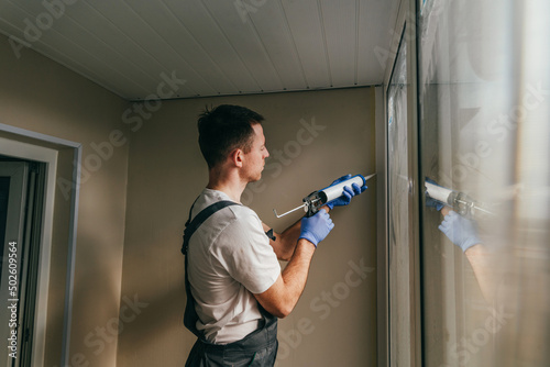Εκτύπωση καμβά Young man wearing overalls sealing cracks between window and trim