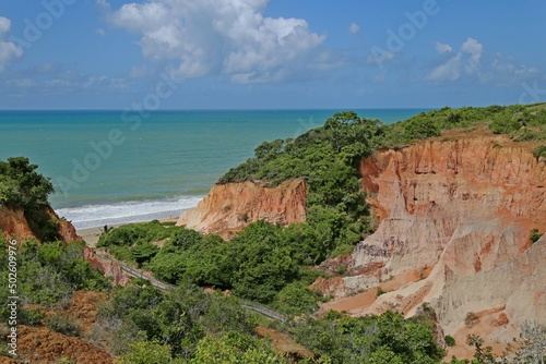 Orange cliff in the middle of green vegetation. In front the sea with small white waves.  horizon  with clam sea.