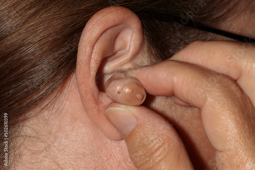 Close-up of a woman's finger inserting a hearing aid in her ear