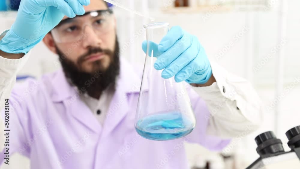 Scientists drop a solution in a lab flask. Makes the blue water in the bottle turn purple. Shake the bottle containing the chemical. a scientist working in a laboratory Scientists drop a solution in a lab flask. Makes the blue water in the bottle turn purple. Shake the bottle containing the chemical. a scientist working in a laboratory