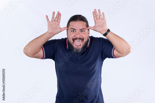 A chubby man in his 30s teasing and mocking someone, sticking his tongue out and taunting with his hands. photo