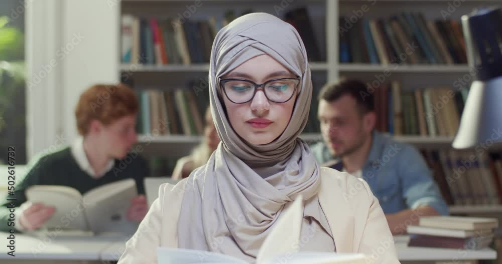 Close up of young Arab muslim woman in hijab and glasses reading book ...