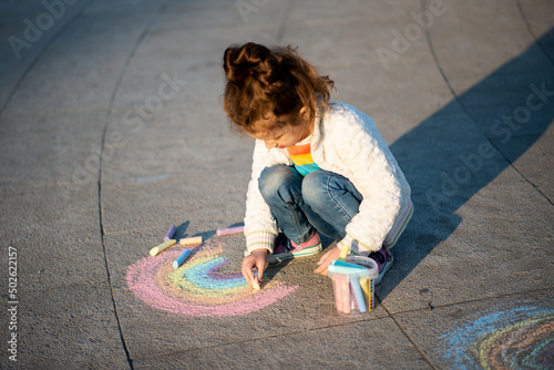 A cute girl draws a rainbow with crayons on the street. Creation. Kids. Street.