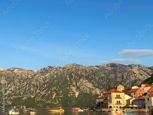 Image of the beautiful buildings in the city of Perast right next to the Perast Beach surrounded by mountains during sunset