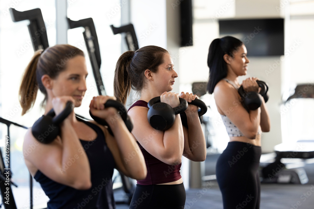 Side view of three young women looking ahead while using kettlebells in gym Side view of three young women looking ahead while using kettlebells in gym