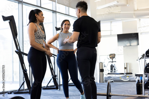 Trainer explain benefits of a workout to two women in gym photo