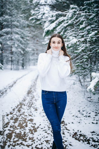 beautiful woman with long hair in a white sweater with a snowy winter forest