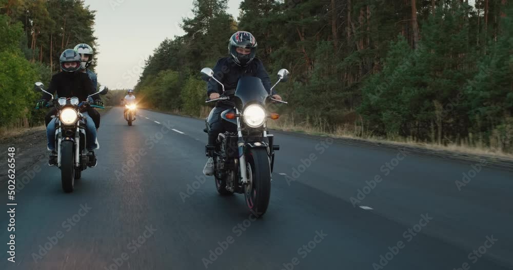 Young travelers ride motorcycles on the highway among high spruces Young travelers ride motorcycles on the highway among high spruces