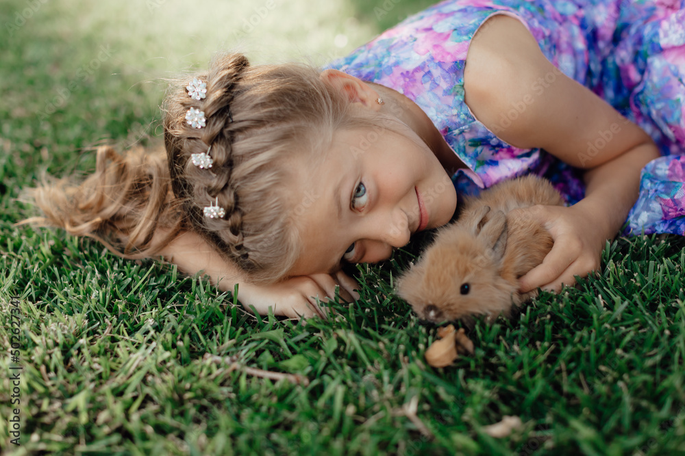 Little girl sitting on the green grass with rabbit. Cute child girl holding a bunny in her hands on Easter day. Little girl sitting on the green grass with rabbit. Cute child girl holding a bunny in her hands on Easter day.