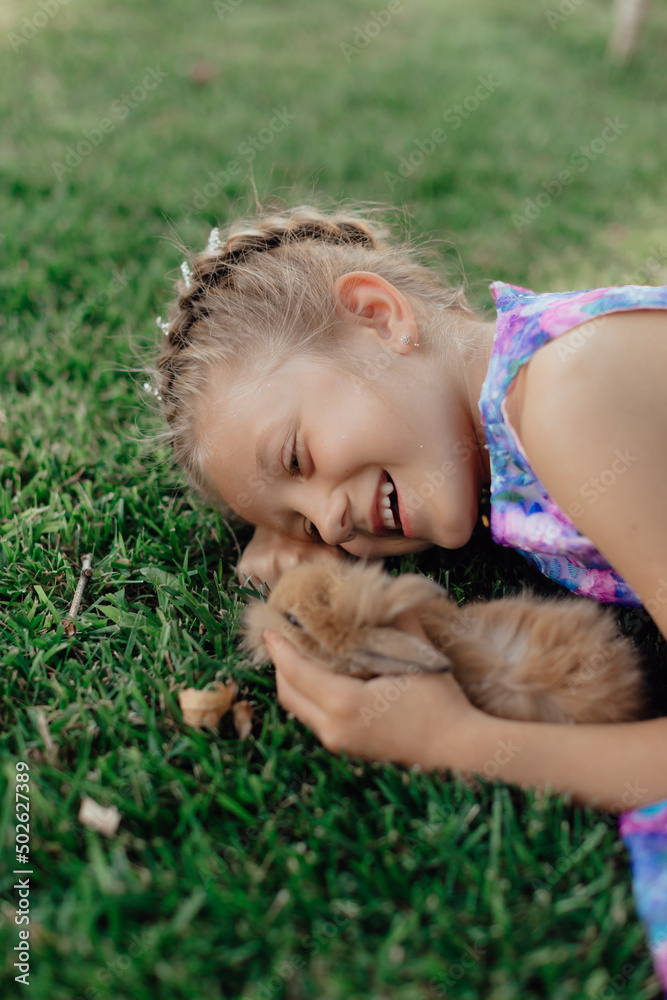 Little girl sitting on the green grass with rabbit. Cute child girl holding a bunny in her hands on Easter day. Little girl sitting on the green grass with rabbit. Cute child girl holding a bunny in her hands on Easter day.
