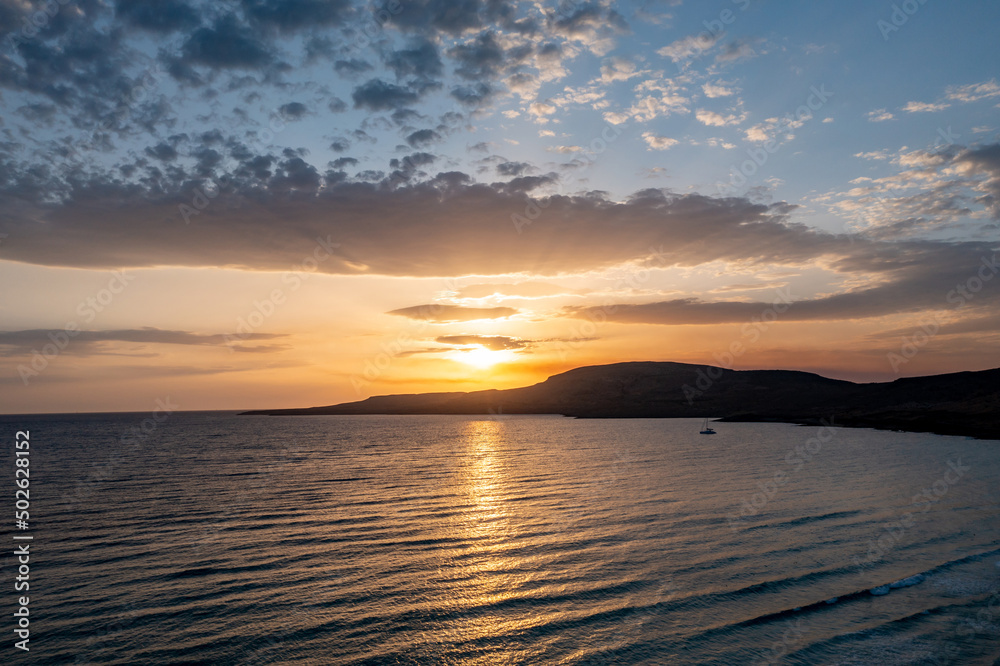 Sunset dramatic sky, Greek island coast. Sun falling over rippled sea water. Calm and peace