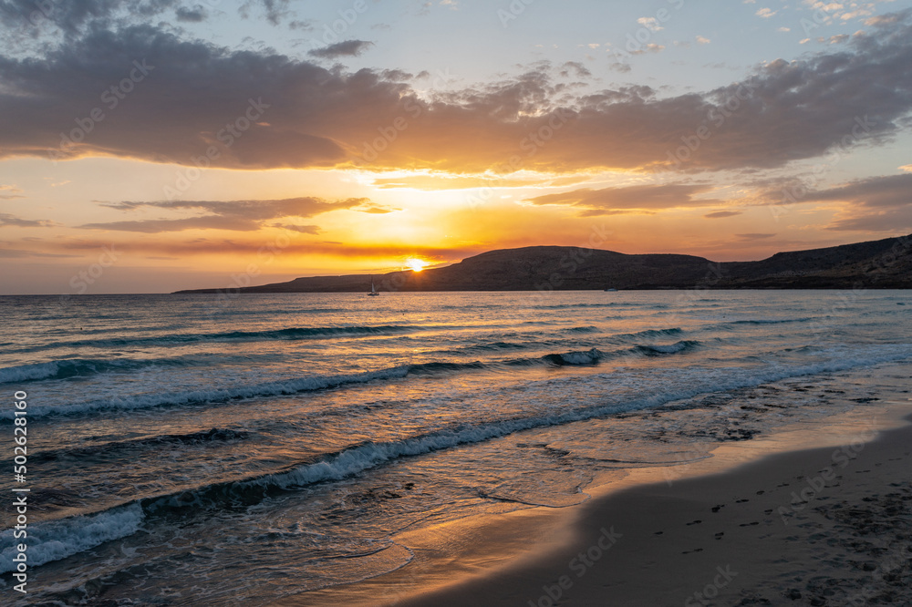 Sunset over empty beach, Elafonisos island, Greece. Small wave on wet sand, colorful cloudy sky