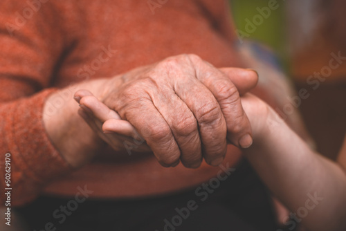 The grandson's hands hold the wrinkled hand of a sick elderly grandmother at home. The concept of love and care. Slow movement