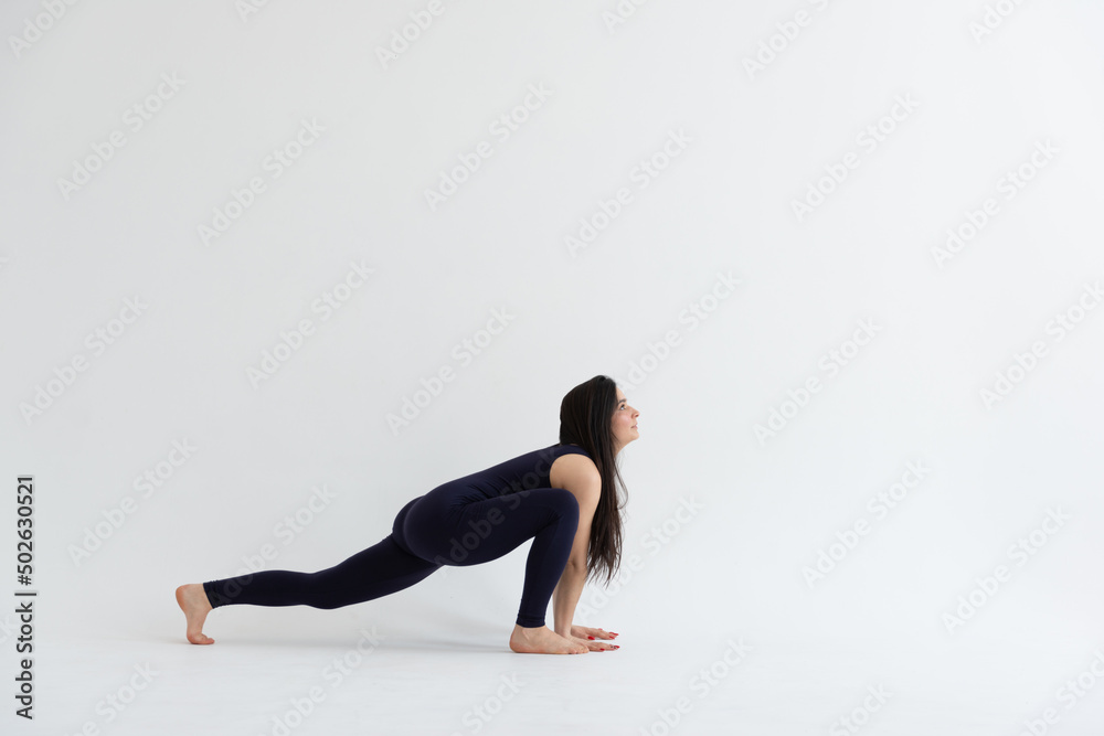 a beautiful young girl with dark hair stands in the pose of Ashva Sanchalasana (with a straight leg) on a white background. Yoga class