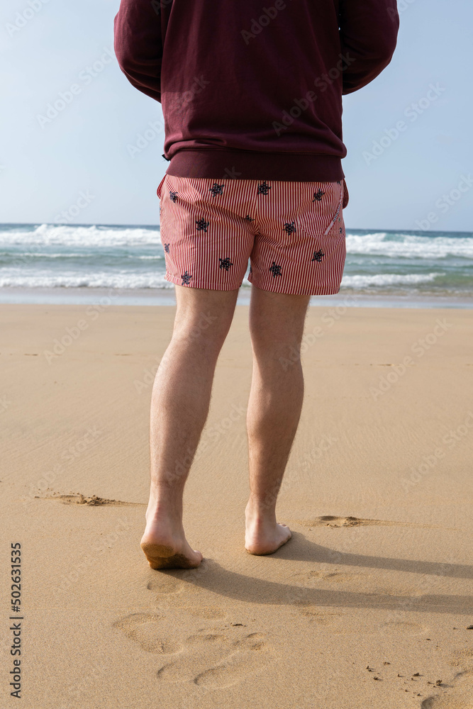 Photo of male legs wearing a swim suit while walking barefoot at the seaside of the beach in summer.