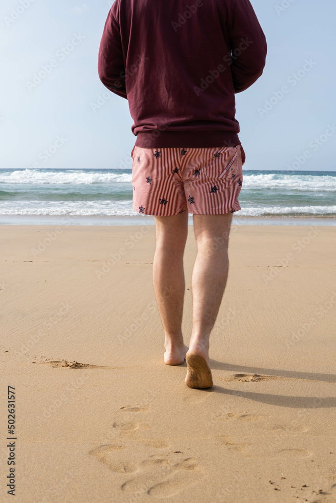 Photo of male legs wearing a swim suit while walking barefoot at the seaside of the beach in summer.
