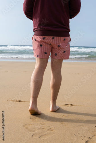 Obraz na płótnie Photo of male legs wearing a swim suit while walking barefoot at the seaside of the beach in summer. w salonie