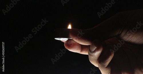 Hand fingers holding one lit burning small decorative oil lamp light with fire flame isolated on dark black night background with copy space. Close up macro side view. soul, worship and hope concept.