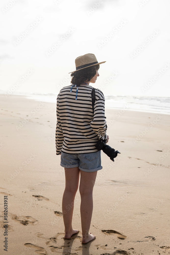 Photo of a young and attractive woman with a photo camera wearing summer clothes at the beach. Photography, holidays, travel. 