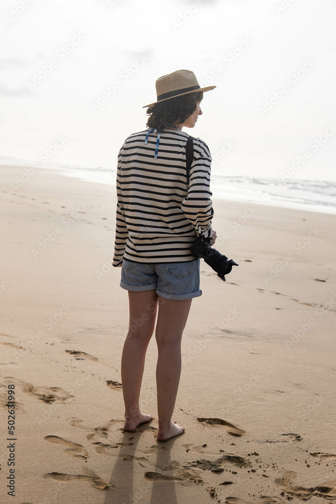 Photo of a young and attractive woman with a photo camera wearing summer clothes at the beach. Photography, holidays, travel.