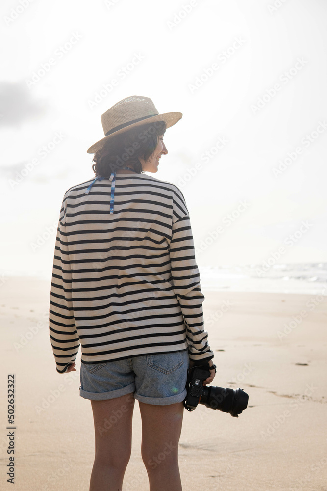 Photo of a young and attractive woman with a photo camera wearing summer clothes at the beach. Photography, holidays, travel. 