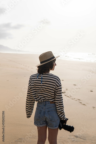 Photo of a young and attractive woman with a photo camera wearing summer clothes at the beach. Photography, holidays, travel. 