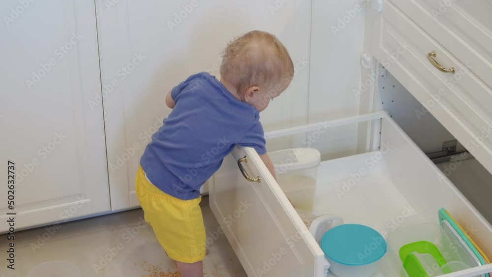 Baby boy having fun playing at home exploring the kitchen, curious toddler opening shelf of the kitchen cabinet taking out kitchen utensils. Infant learn exploring environment. High quality 4k footage Baby boy having fun playing at home exploring the kitchen, curious toddler opening shelf of the kitchen cabinet taking out kitchen utensils. Infant learn exploring environment. High quality 4k footage