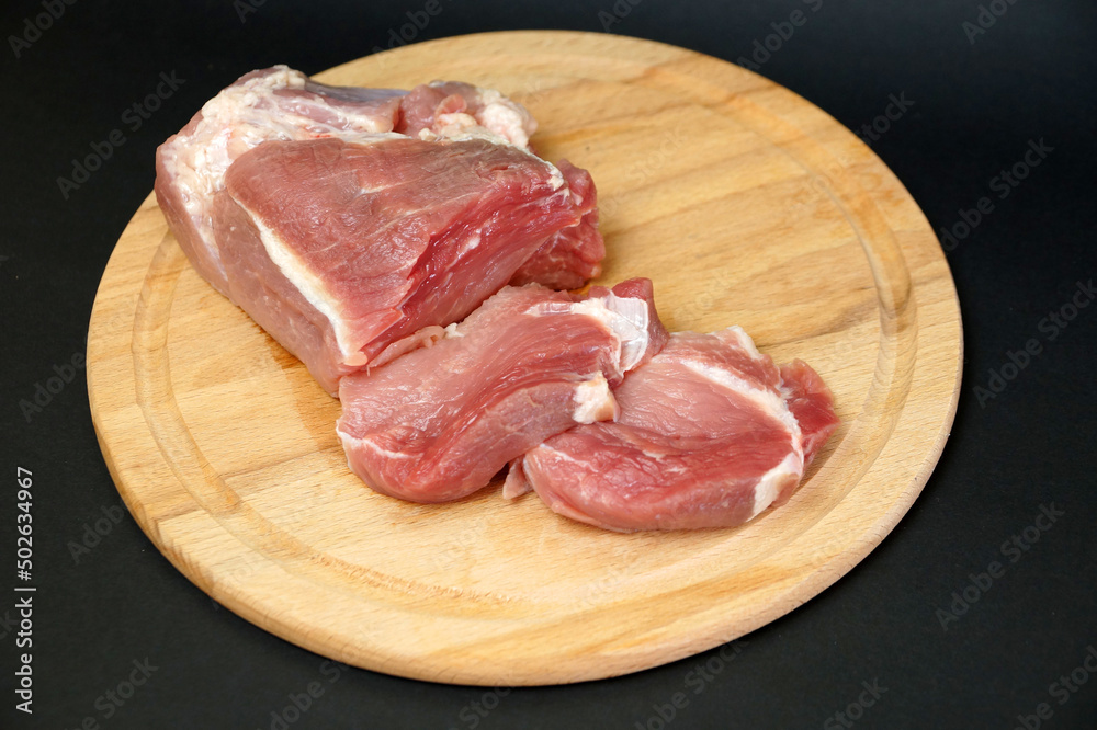 sliced raw pork fillet on a cutting board on a black background
