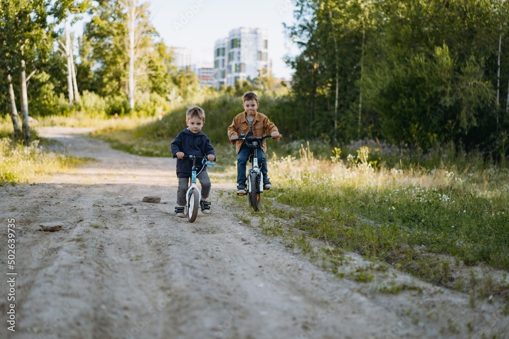 cute caucasian boys brothers are cycling together in countryside in summer time. Little one is riding runbike, elder one riding bicycle. Image with selective focus