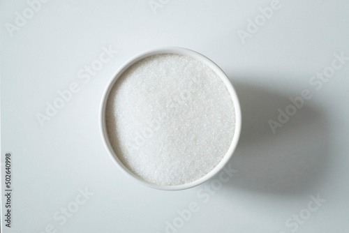 Granules of white sugar in a bowl on a white background