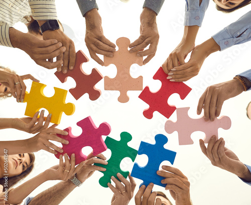 Teamwork. Pieces of colored puzzle in the arms of people standing in a circle and connecting them. Team is looking for a way to solve the problem by studying for business training. Bottom view.