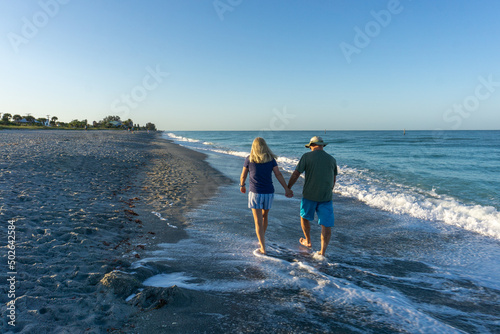 Retired couple walk down beach at sunrise in Florida