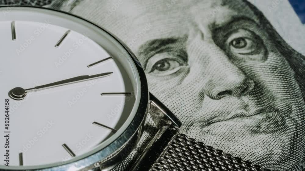 Timelapse of silver steel mechanical clock on 100 dollars background. Chronograph close up with hour and minute hand. Womens watch. Time, finance, business concept