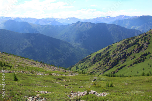Green rocky slopes of high mountains with a distant view of the huge mountain ranges in Altai at the Karatyurek pass, panoramic view, sky with clouds