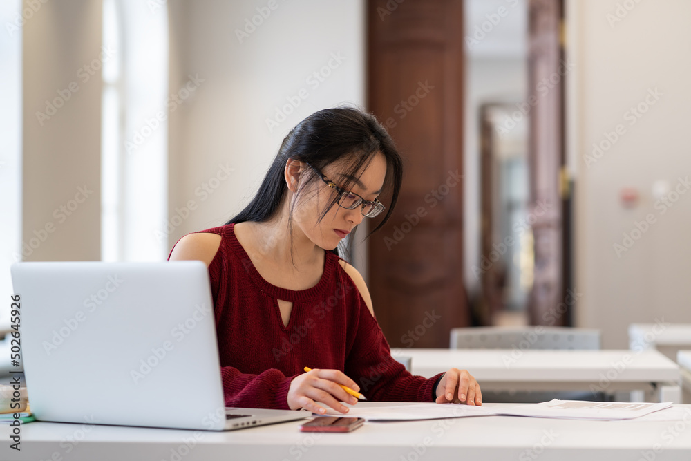 Focused asian female student sitting at library desk with laptop, preparing for exam or doing homework with internet. Concentrated japanese college girl studying in university reading room Focused asian female student sitting at library desk with laptop, preparing for exam or doing homework with internet. Concentrated japanese college girl studying in university reading room